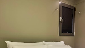 Un lit avec une literie blanche, dans une pièce dotée d’une fenêtre et d’une porte.