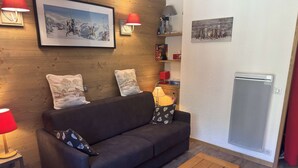 A modern living room with a dark sofa, wooden floor, and a small wooden table. There are wall-mounted lamps and a framed picture above the sofa.