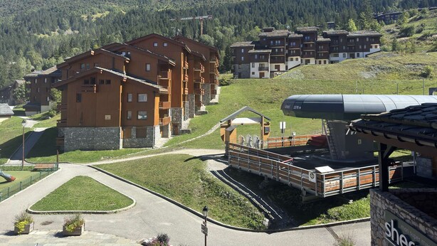 A hotel with multiple wooden buildings, a ski lift, and a mountainous backdrop.