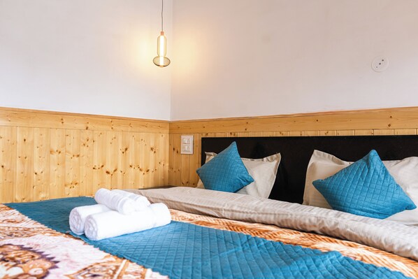 Una habitación de hotel con cabecera de madera, cama con ropa de cama azul y blanca, y una colcha azul acolchada.