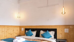A neatly made bed with blue and white bedding, a wooden headboard, and two pendant lights hanging from the ceiling. - Story Homes- Deluxe Room (Kaza Khas)