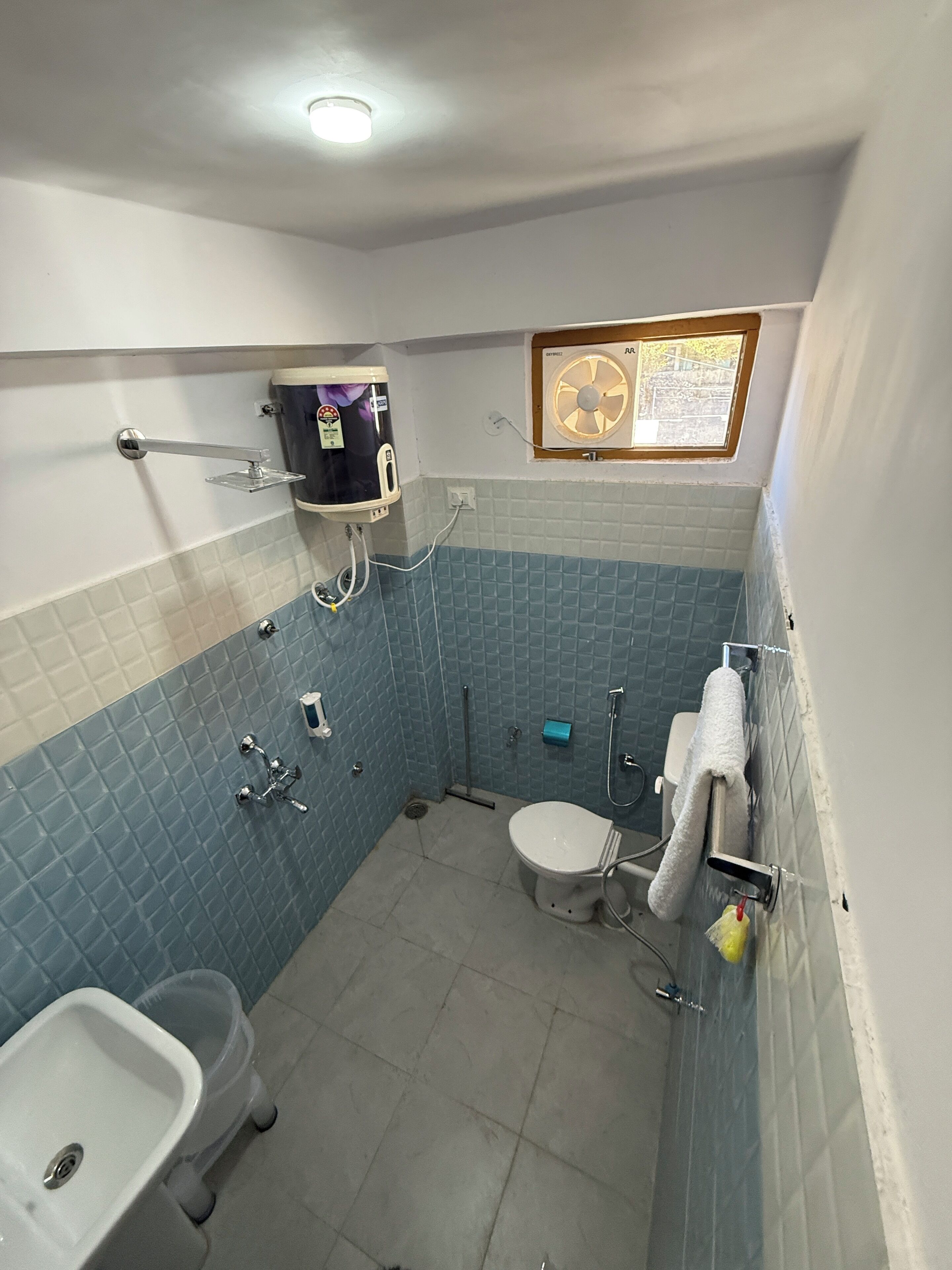 Ein Badezimmer mit Toilette, Waschbecken, Dusche und einem an der Wand befestigten Ventilator.