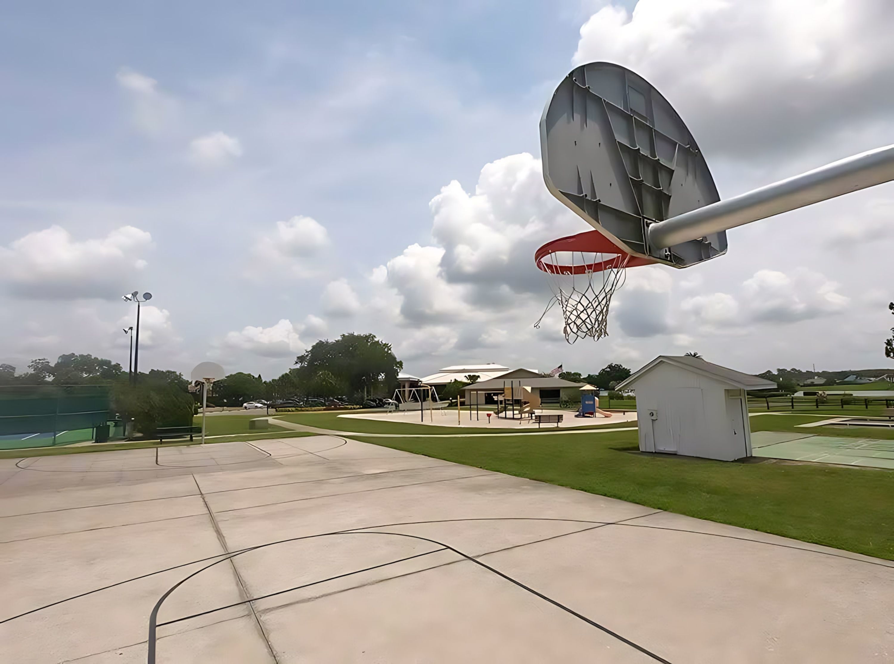 A basketball court with a hoop, a small shed, and a covered seating area.