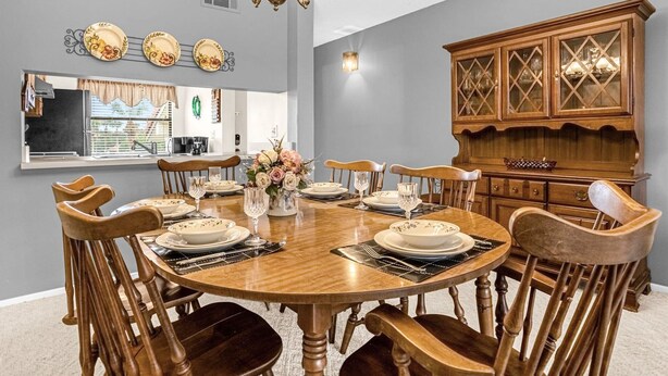 A dining room with a round wooden table set for six, surrounded by six wooden chairs. A chandelier hangs from the ceiling, and a wooden cabinet with glass doors is to the right. - Upstay 2BR Golfer s Retreat w Patio Ventura Resort (Orlando)