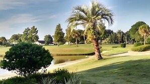 A golf course with a pond, palm trees, and a well-maintained lawn. - Upstay 2BR Golfer s Retreat w Patio Ventura Resort (Orlando)
