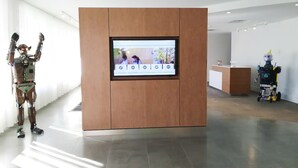 Un espace d’accueil comprenant un comptoir de réception en bois, un écran numérique et un robot.