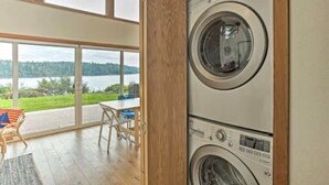 A laundry room with two stacked washing machines, large windows, and a view of a lake.