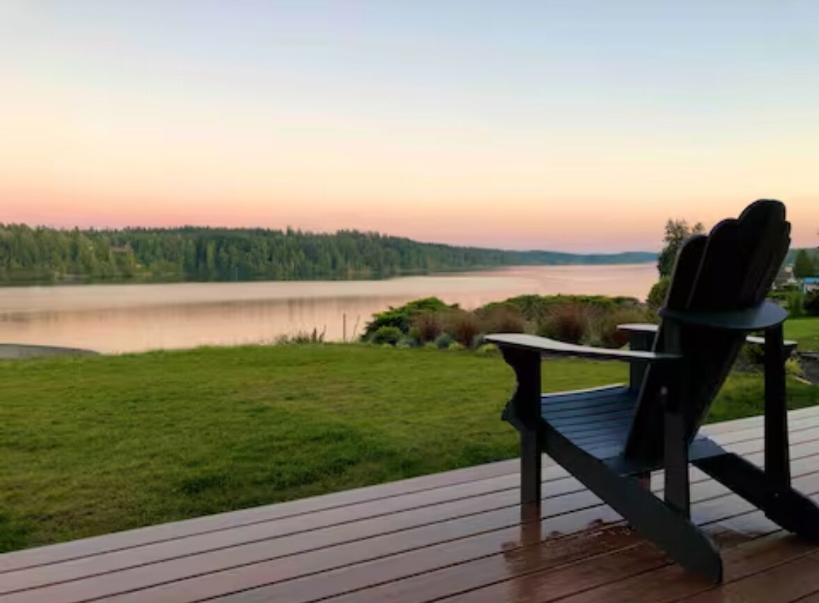 Una terraza con una silla que da a un lago al atardecer.