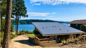 A cabin with a metal roof, situated by a lake with a forest backdrop.