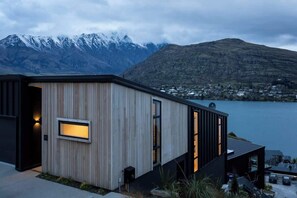 Un edificio moderno con fachada de madera, ventanas amplias y vistas a un lago y montañas.