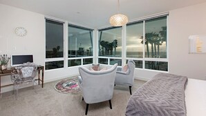 Quarto moderno com janelas amplas, escrivaninha, duas poltronas e uma cama.