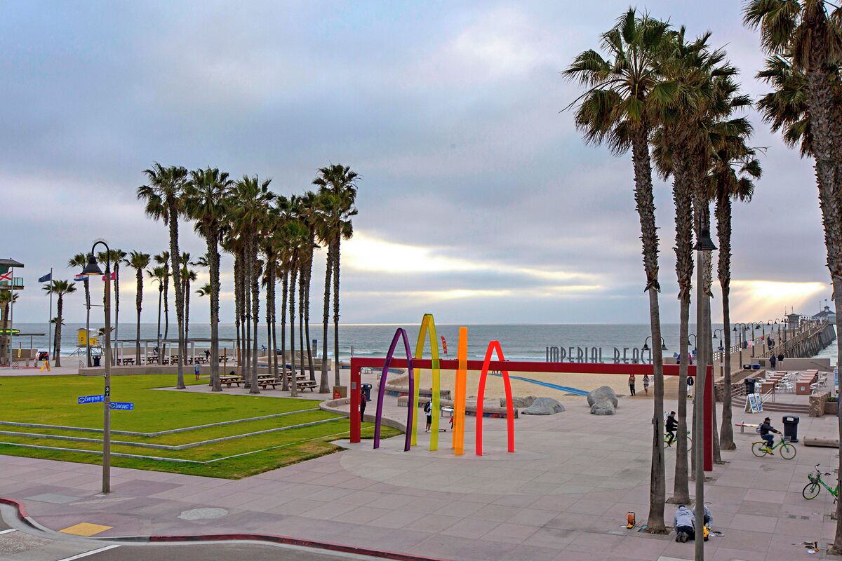 A coastal promenade with palm trees, a pedestrian walkway, and a colorful sculpture.