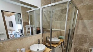 A modern bathroom with a glass shower enclosure, two sinks, a wooden vanity, and a large mirror. - Furnished studio with all comforts (Beaumont-en-Véron)