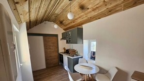 A compact kitchen with wooden ceiling beams, a small dining area with two chairs, and a window with a view. - Furnished studio with all comforts (Beaumont-en-Véron)