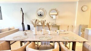 Zona pranzo con tavolo in marmo, sedie beige rivestite in tessuto, vasi decorativi con piante essiccate e specchi a parete.