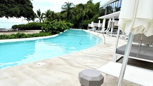 A swimming pool with lounge chairs and umbrellas, surrounded by greenery and a building with large windows. - Bolongo 3BR Your Exclusive Oceanfront Escape (Punta de Mita)