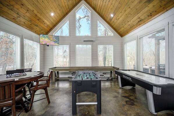 A spacious room with a foosball table, pool table, and a television mounted on the wall.