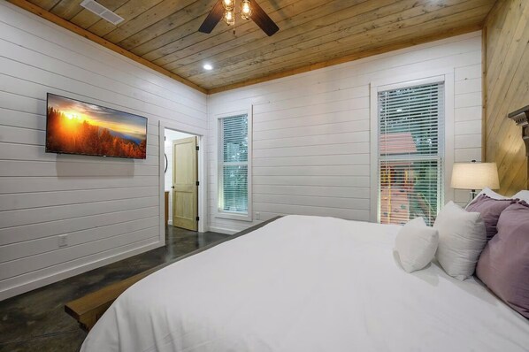 A bedroom with a large bed, a TV mounted on the wall, and a ceiling fan.