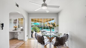 A modern dining area with a glass table, clear chairs, and a ceiling fan.
