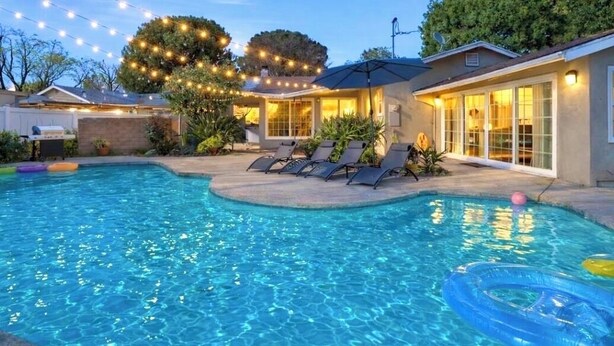A swimming pool with lounge chairs, string lights, and a covered patio area.
