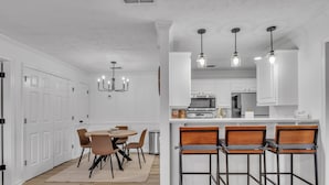 Una cocina moderna con armarios blancos, una isla central con taburetes y lámparas colgantes.