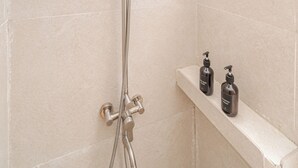 Una dutxa amb plat de roba flexible i aixeta fixada a la paret, una prestatgeria amb dues amples, i una paret amb rajoles.