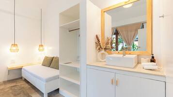 Un dormitorio moderno con cama, lámparas de noche, armario y baño con lavabo, espejo y toalla.
