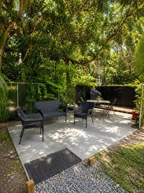 An outdoor patio area with wicker furniture, a concrete floor, and a metal grill.