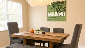 Uma sala de jantar com mesa de madeira, cadeiras estofadas cinzentas, um banco e um lustre decorativo.