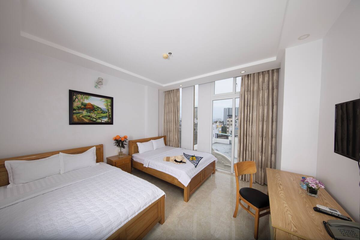 Une chambre d’hôtel avec deux lits, un bureau, une chaise, une télévision et un balcon avec des rideaux.