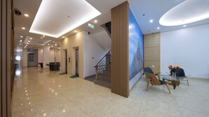 A modern hotel lobby with a marble floor, a staircase, and a reception desk with chairs and a vase of flowers. - Oceanic Hotel Vung Tau (Ho Chi Minh City)