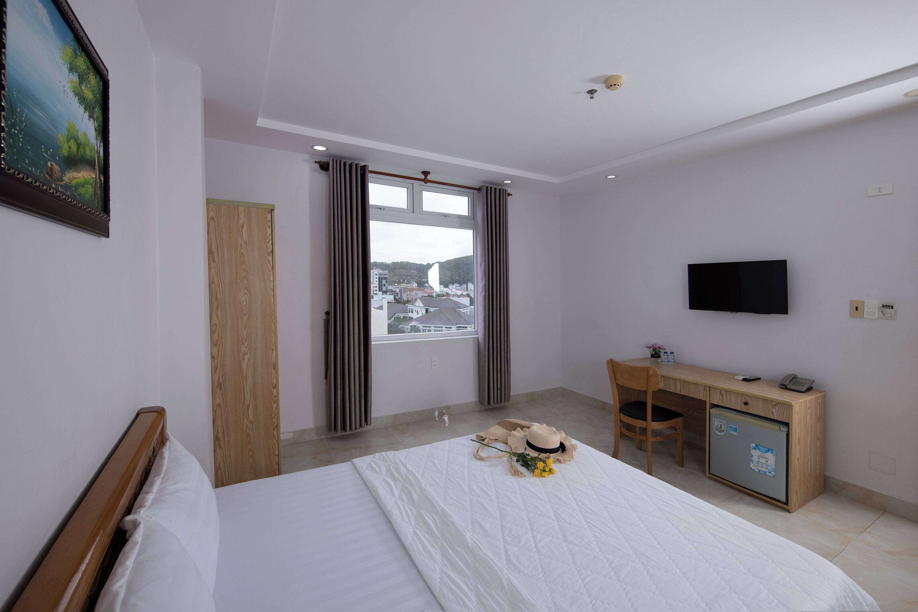 A hotel room with a bed, a desk, a TV, and a window with curtains.