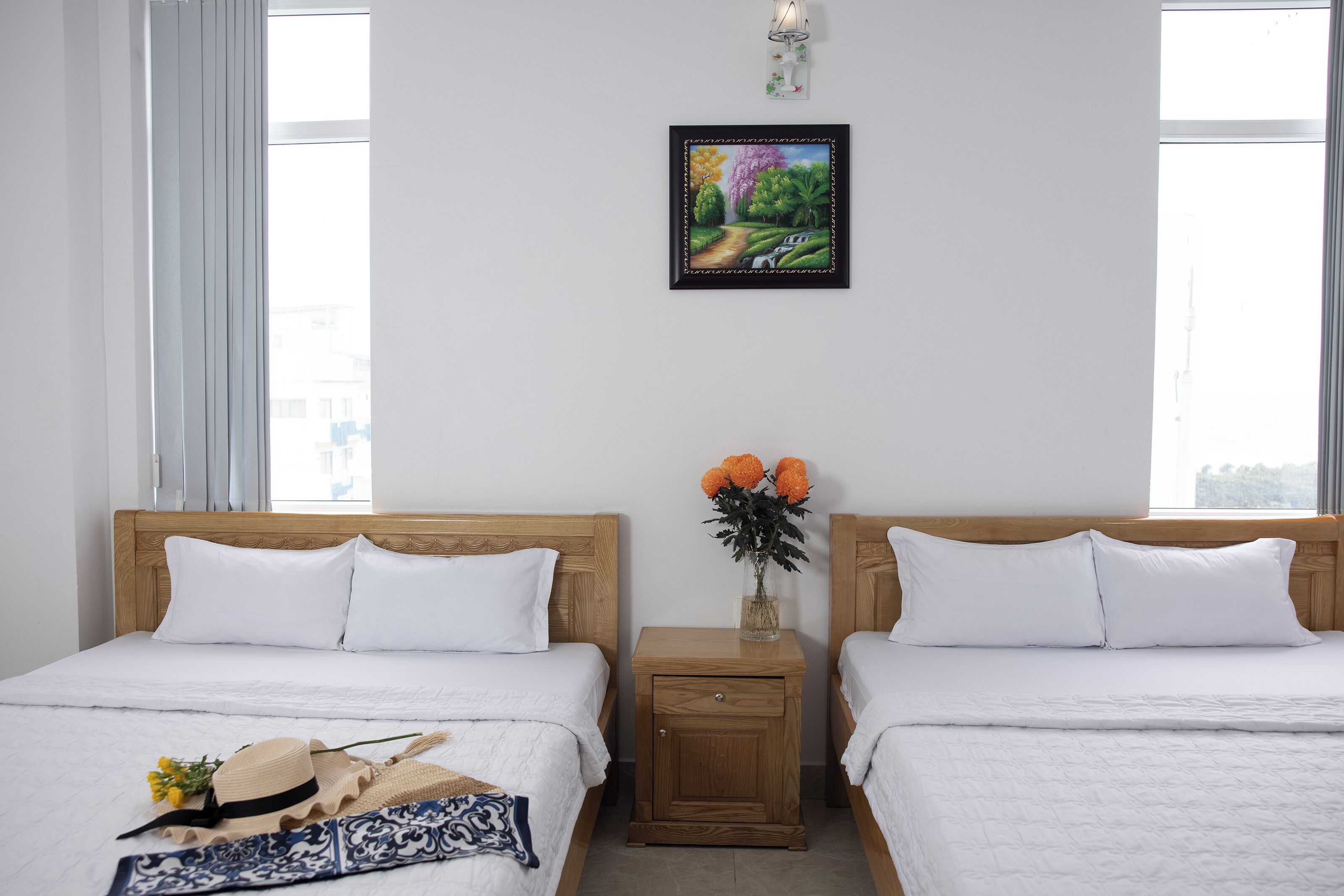 A hotel room with two beds, a nightstand with a vase of flowers, and a framed picture on the wall.