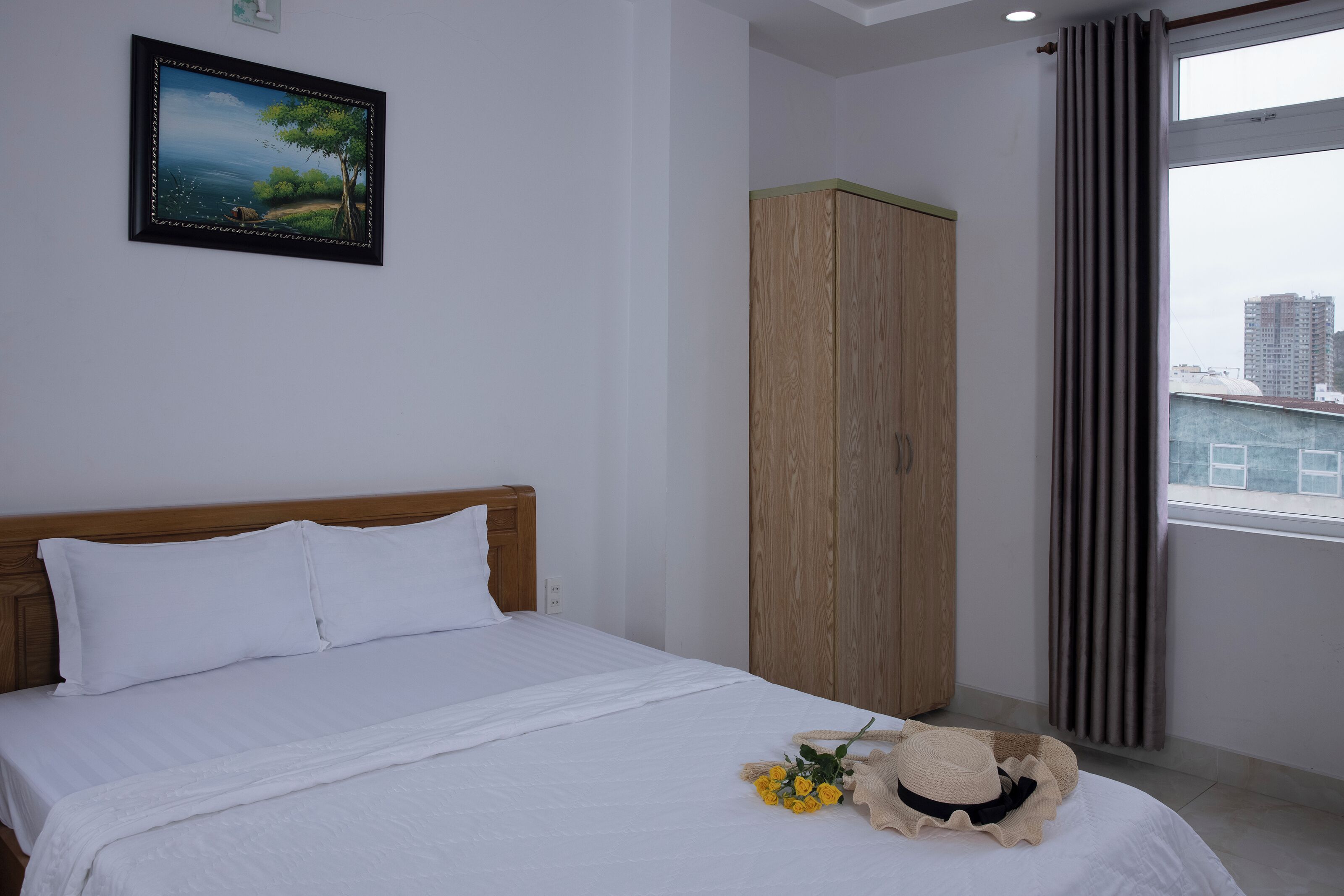 Un dormitorio con cama, armario, ventana con cortinas y un cuadro en la pared.