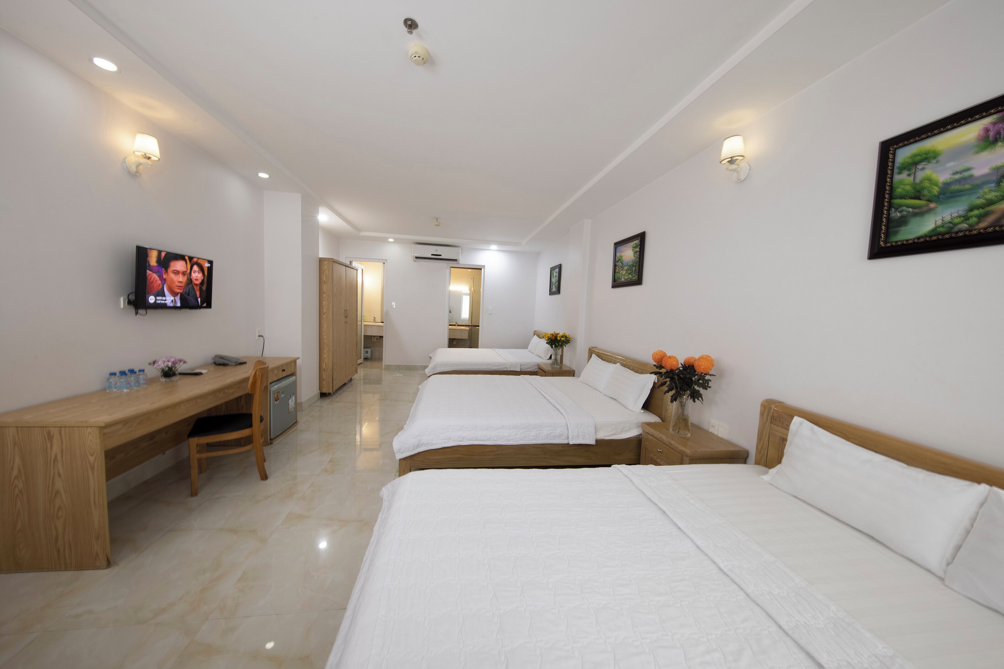 A hotel room with two beds, a desk, a TV, and a bathroom visible in the background.