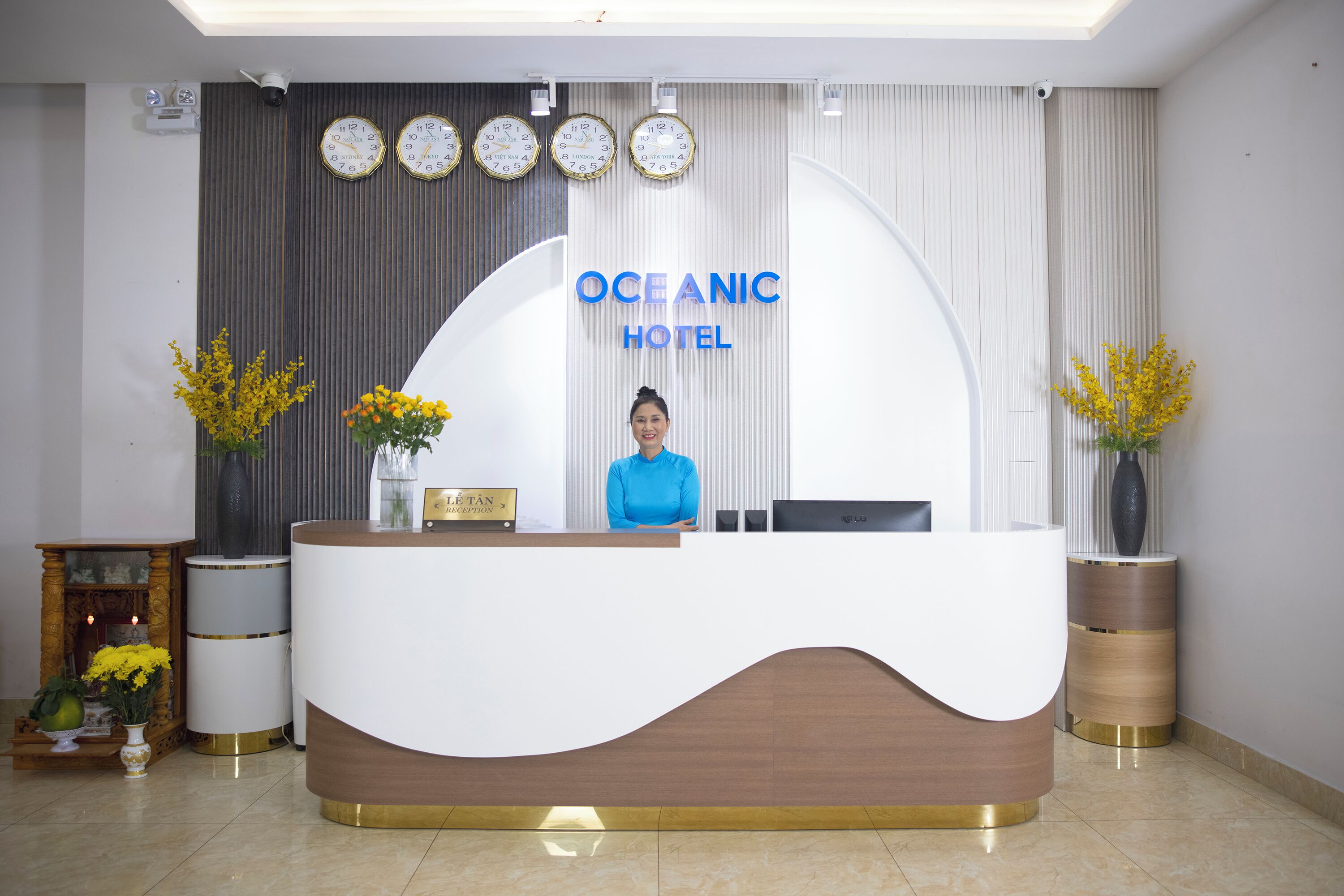 A reception desk at the Oceanic Hotel with a receptionist, clocks, and decorative vases.