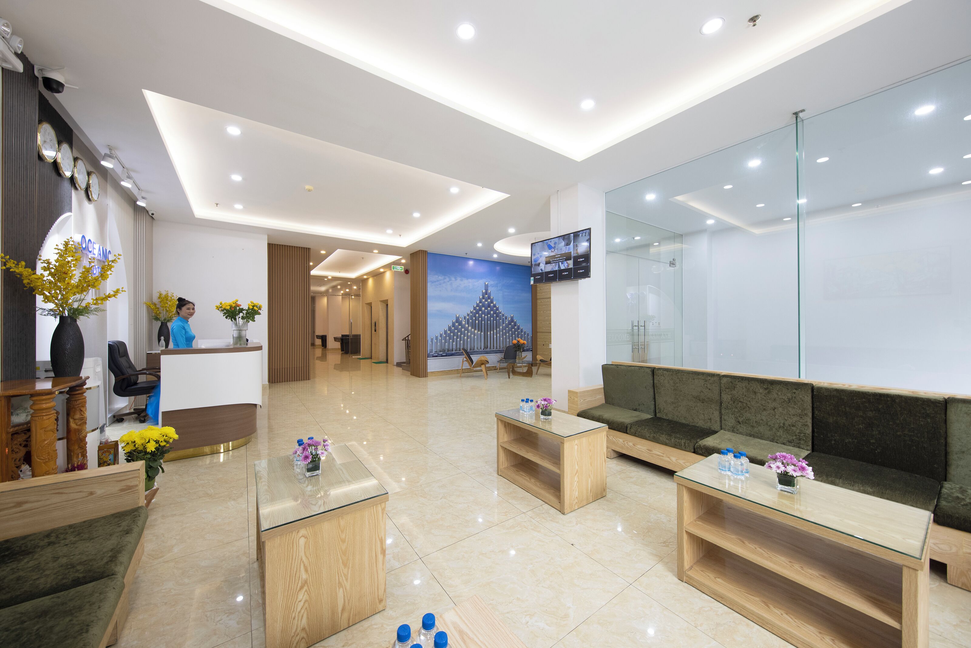 A modern hotel lobby with a reception desk, seating area, and a large digital screen.