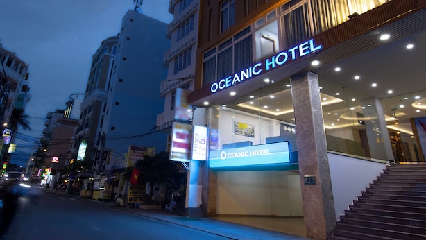 The exterior of Oceanic Hotel with a prominent sign, a staircase leading to the entrance, and a street view with other buildings and signs. - Oceanic Hotel Vung Tau (Ho Chi Minh City)