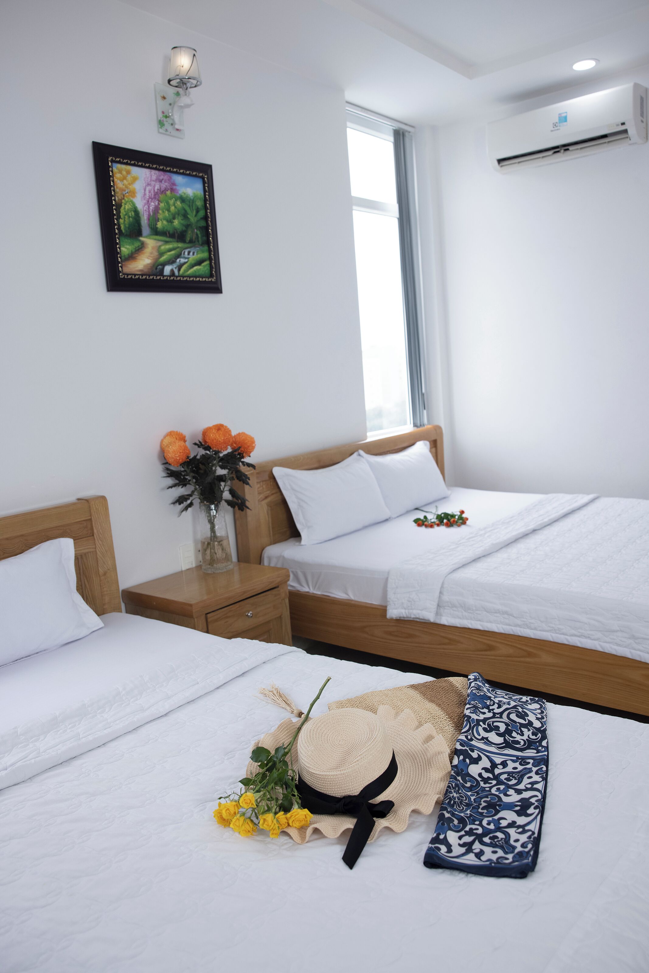 Ein Hotelzimmer mit zwei Betten, einem Nachttisch, einer Blumenvase und einem gerahmten Bild an der Wand.