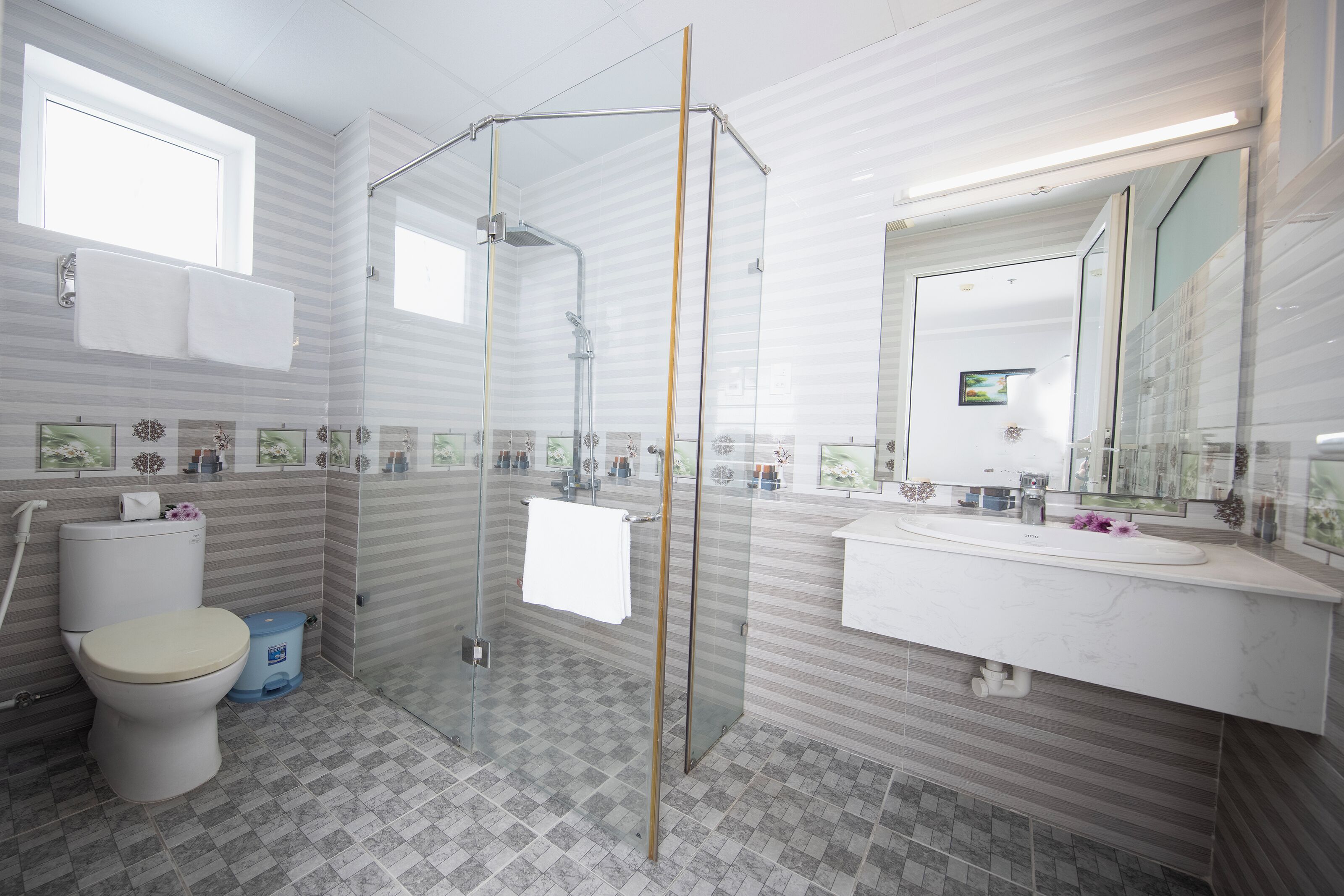 Un baño moderno con ducha de vidrio, inodoro y lavamanos con espejo superior.