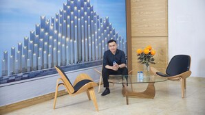 A modern reception area with a glass table, two wooden chairs, a vase with flowers, and a large cityscape mural on the wall. - Oceanic Hotel Vung Tau (Ho Chi Minh City)