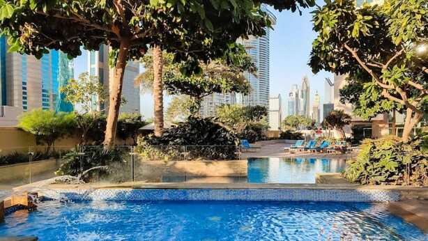 Une piscine à l’eau d’un bleu cristallin, entourée d’une végétation luxuriante et avec de grands immeubles en arrière-plan.