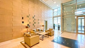 Un hall d’entrée au design moderne, comprenant un espace salon avec des canapés et une table basse, un mur décoré de motifs et de grandes portes vitrées donnant sur l’extérieur.
