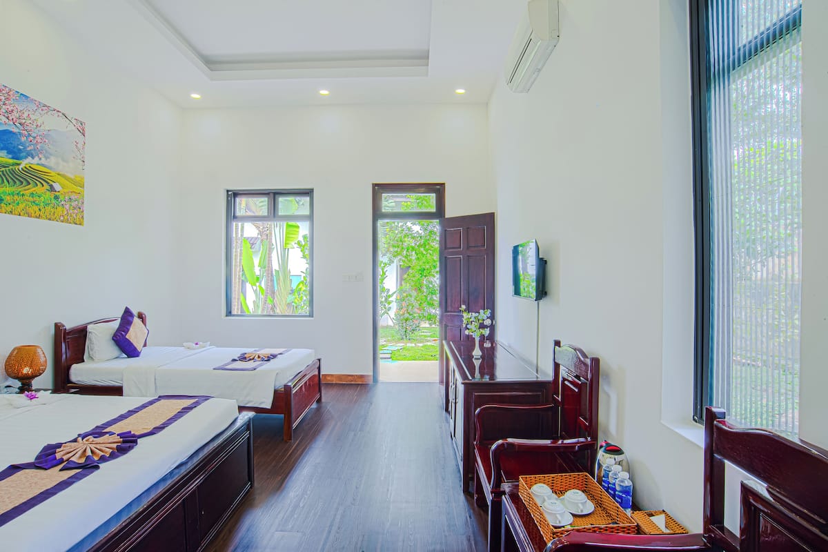 A hotel room with two beds, a dining table, a TV, and a view of the garden.
