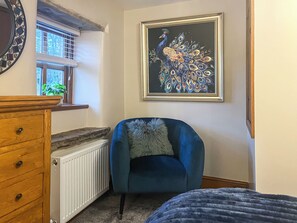 A room with a blue armchair, a wooden dresser, a radiator, and a framed peacock painting on the wall. - 2 bedroom accommodation in Barnoldswick (Barnoldswick)