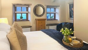 Une chambre à coucher comprenant un lit, une commode, deux fenêtres, un miroir et une table de chevet ornée d’un vase de fleurs.