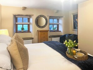A bedroom with a bed, dresser, two windows, a mirror, and a bedside table with a vase of flowers. - 2 bedroom accommodation in Barnoldswick (Barnoldswick)