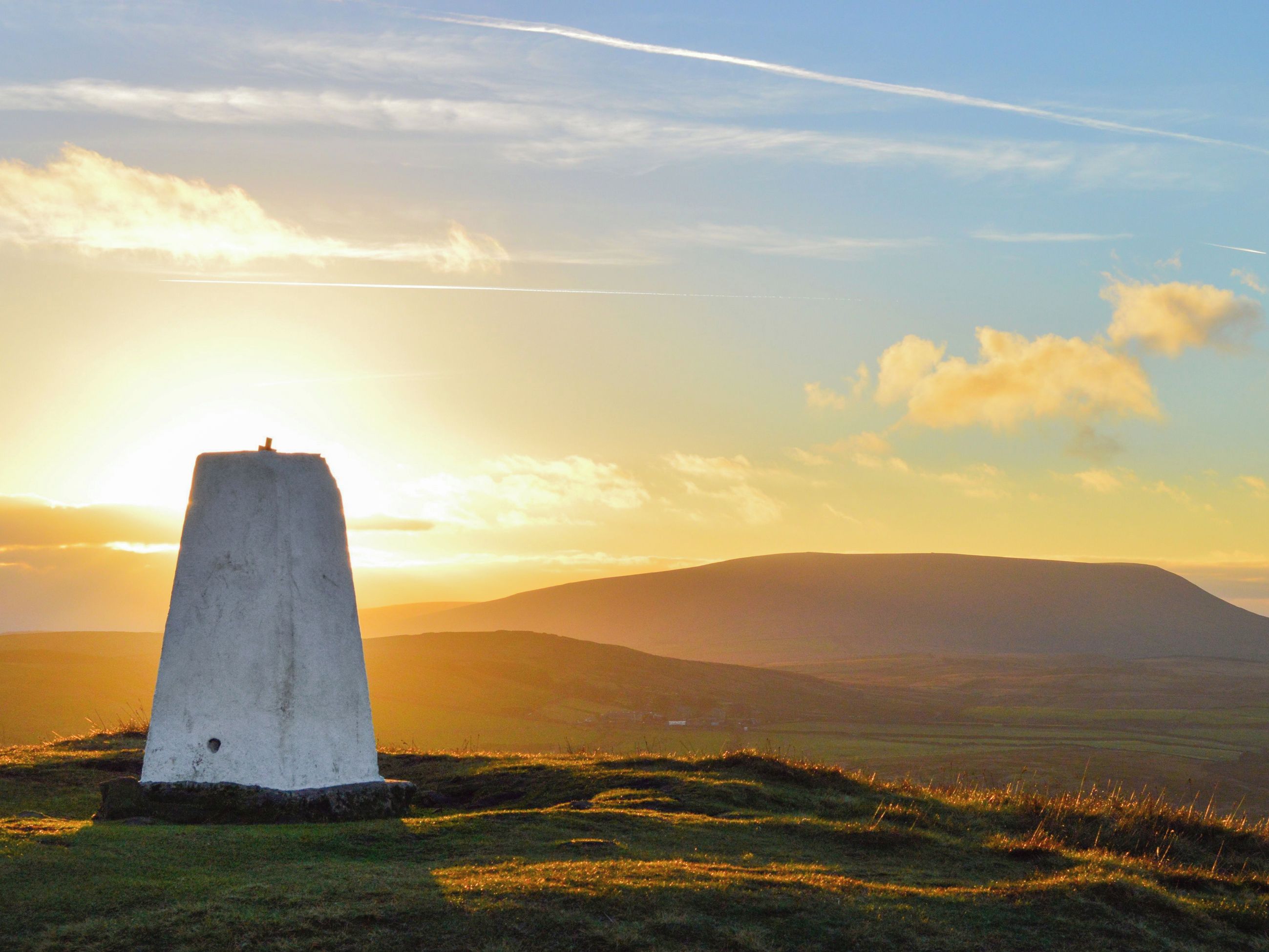 A solitary concrete monument in a grassy field with a sunset in the background.