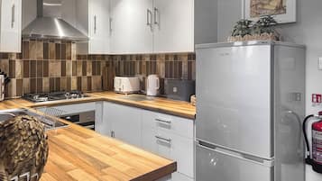 A modern kitchen with white cabinets, a stainless steel range hood, a wooden countertop, and a stainless steel refrigerator.
