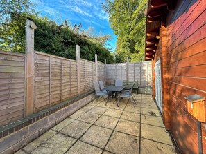 A patio with a table and chairs, a wooden fence, and a brick border.